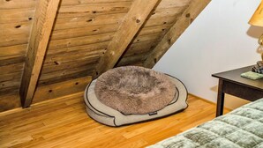 Un panier pour animal de compagnie dans une pièce dont le plafond est orné de poutres en bois et le sol est recouvert de planches de bois.