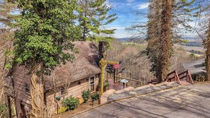 Un chalet rustique avec une cheminée en pierre, une véranda dotée d’une balustrade et une vue sur le paysage environnant.
