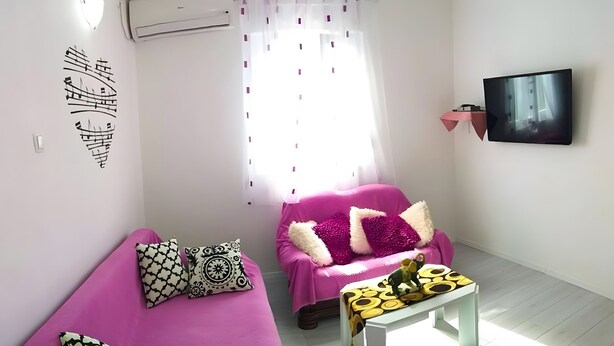 A living room with a pink sofa, a white coffee table, and a flat-screen TV mounted on the wall. - Apartment 'Čagalj Trogir' with Sea View, Wi-Fi and Air Conditioning (Trogir)