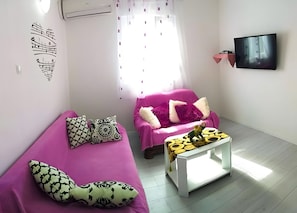 A living room with a pink sofa, a white coffee table, and a flat-screen TV mounted on the wall. - Apartment 'Čagalj Trogir' with Sea View, Wi-Fi and Air Conditioning (Trogir)