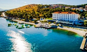 A coastal hotel with a large building, a beach, and a clear blue sea. - Apartment 'Čagalj Trogir' with Sea View, Wi-Fi and Air Conditioning (Trogir)