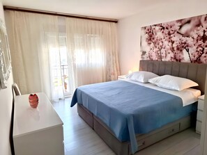 Ein Schlafzimmer mit einem Bett, einem Nachttisch, einem Sessel und einem Fenster mit Vorhängen.