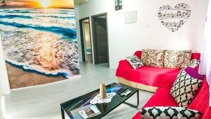 A living room with a red sofa, patterned cushions, a glass coffee table with magazines, and a wall mural of a beach scene. - Apartment 'Čagalj Trogir' with Sea View, Wi-Fi and Air Conditioning (Trogir)