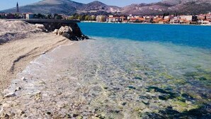 A beach with clear water, a rocky shoreline, and a town in the background. - Apartment 'Čagalj Trogir' with Sea View, Wi-Fi and Air Conditioning (Trogir)