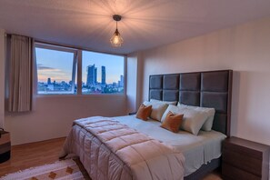 Ein Schlafzimmer mit Blick auf die Stadt, ein großes Bett mit vielen Kissen, ein Kopfteil und eine hängende Leuchte.
