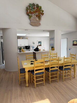 Ein Essbereich mit einem Holztisch und -stühlen, im Hintergrund eine Küche und ein dekoratives Wandbild über dem Tisch.
