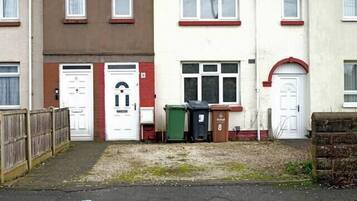 A row of terraced houses with front doors, a small garden area, and a street in front.