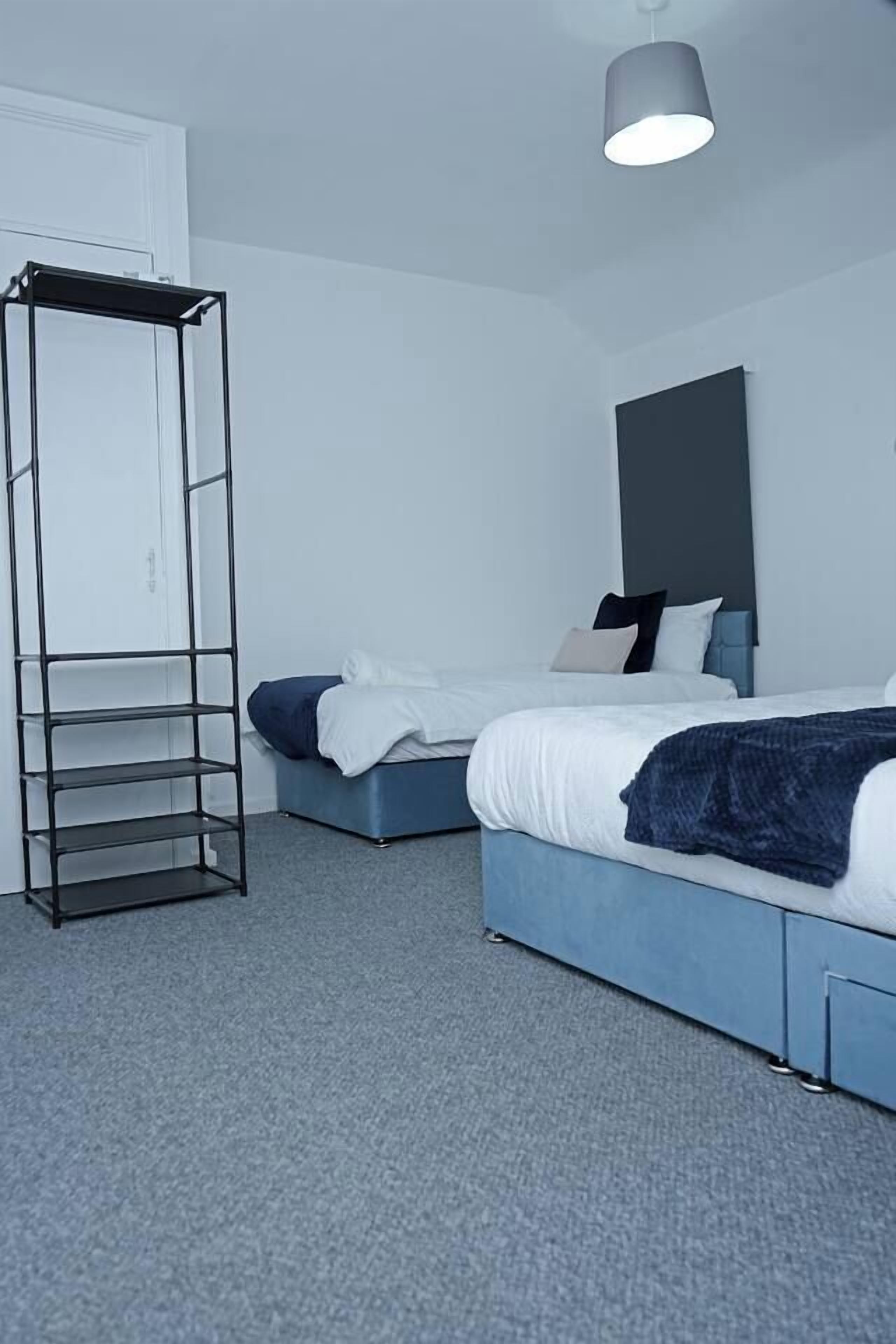 Een slaapkamer met twee bedden, een metalen open kast en een plafondlamp.