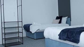 Een slaapkamer met twee bedden, een metalen open kast en een plafondlamp.