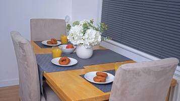 Ein Esstisch mit Frühstücksangeboten, darunter Gebäck und Saft, sowie eine Vase mit weißen Blumen.