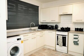 A compact kitchen with a washing machine, a stove, and a sink.
