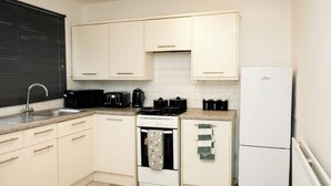 Una cocina compacta con armarios blancos, estufa, lavaplatos y refrigerador.