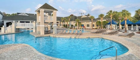 A swimming pool with lounge chairs and a covered area, surrounded by buildings.