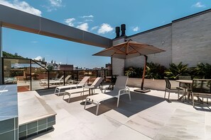 An outdoor patio with lounge chairs, a table, and an umbrella. - Sunrise Residence (Bombinhas)