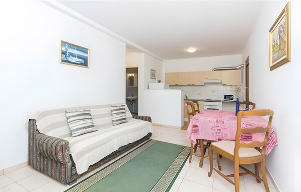 Ein kompakter Wohnbereich mit einer Couch, einem Esstisch mit Stühlen, einer Küchenzeile und einem gerahmten Bild an der Wand.
