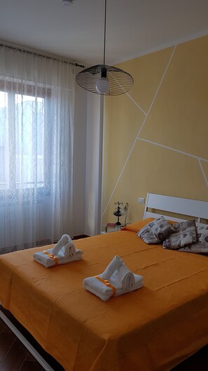 A neatly made bed with towels, a bedside table with a lamp, and a window with sheer curtains. - CASA MIA Guesthouse (Firenze)