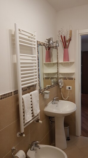 A bathroom with a white sink, a towel rack with a white towel, a mirror with a pink vase, and a hairdryer on the wall. - CASA MIA Guesthouse (Firenze)