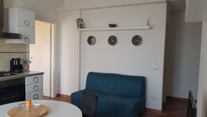 A modern kitchen with a built-in stove, a coffee maker, and a dining area with a round table and a teal sofa. - CASA MIA Guesthouse (Firenze)