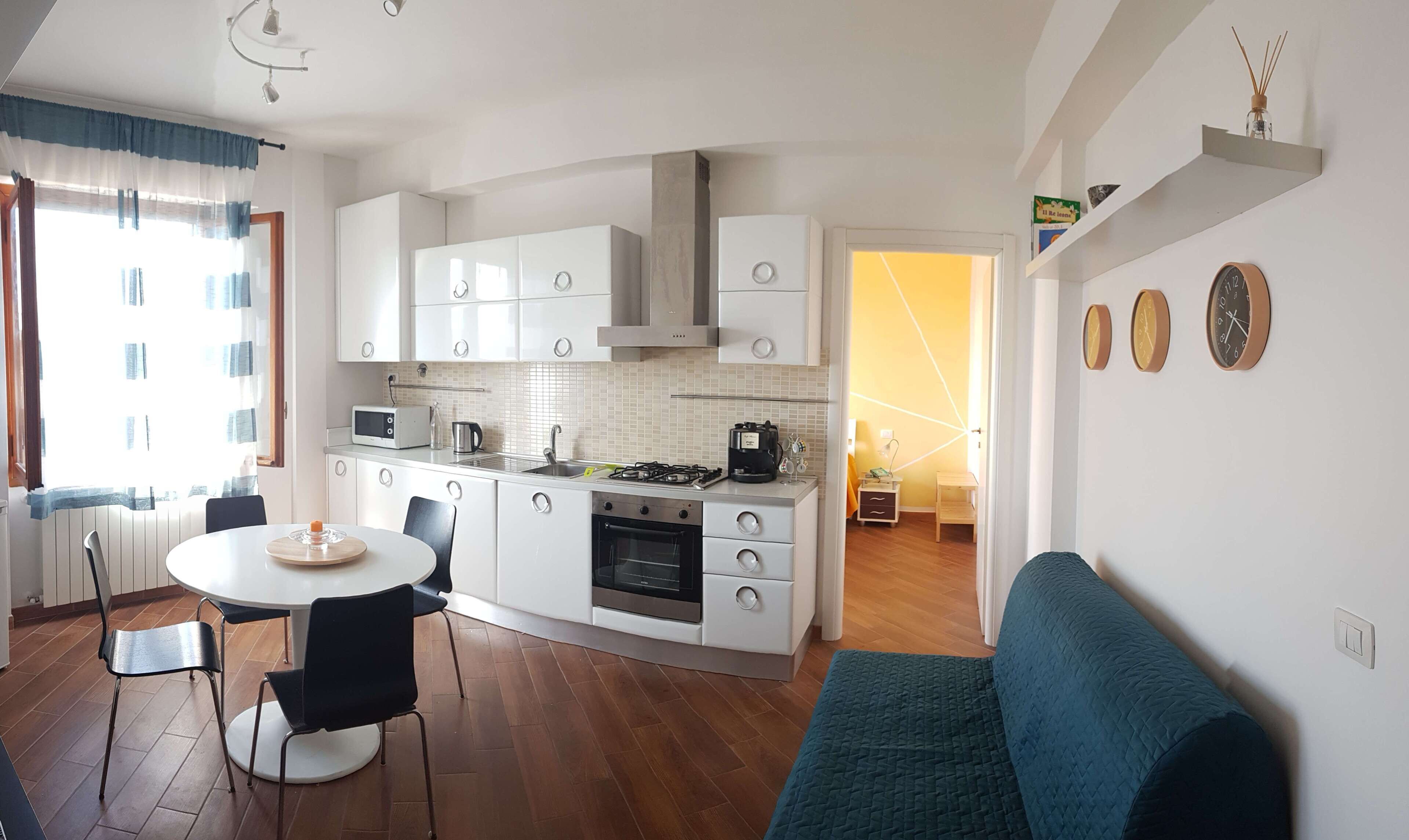 A modern kitchen with white cabinets, a gas stove, and a microwave. There is a dining area with a round table and chairs.