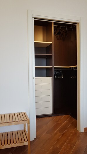 A walk-in closet with open shelves, a wooden bench, and a dark closet door. - CASA MIA Guesthouse (Firenze)