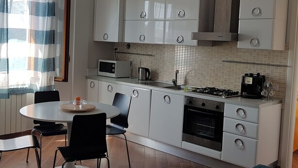 A modern kitchen with white cabinets, a gas stove, a microwave, and a dining area with a table and chairs. - CASA MIA Guesthouse (Firenze)