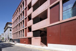 A modern building with a red facade, multiple windows, and a visible entrance with a metal gate. - Aspasios Formosa Collection (Porto)