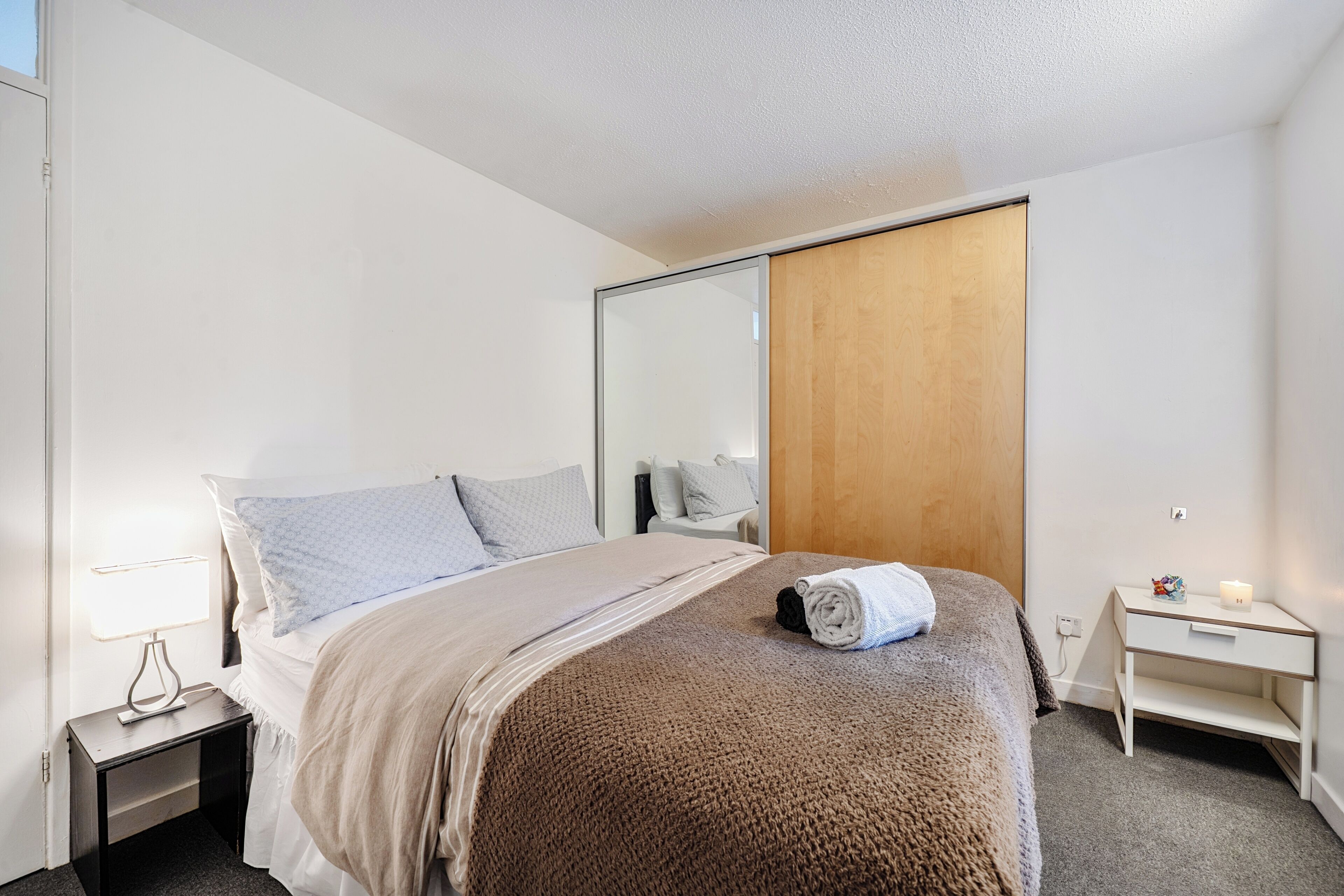 A hotel room with a bed, bedside table, lamp, and a wooden wardrobe.