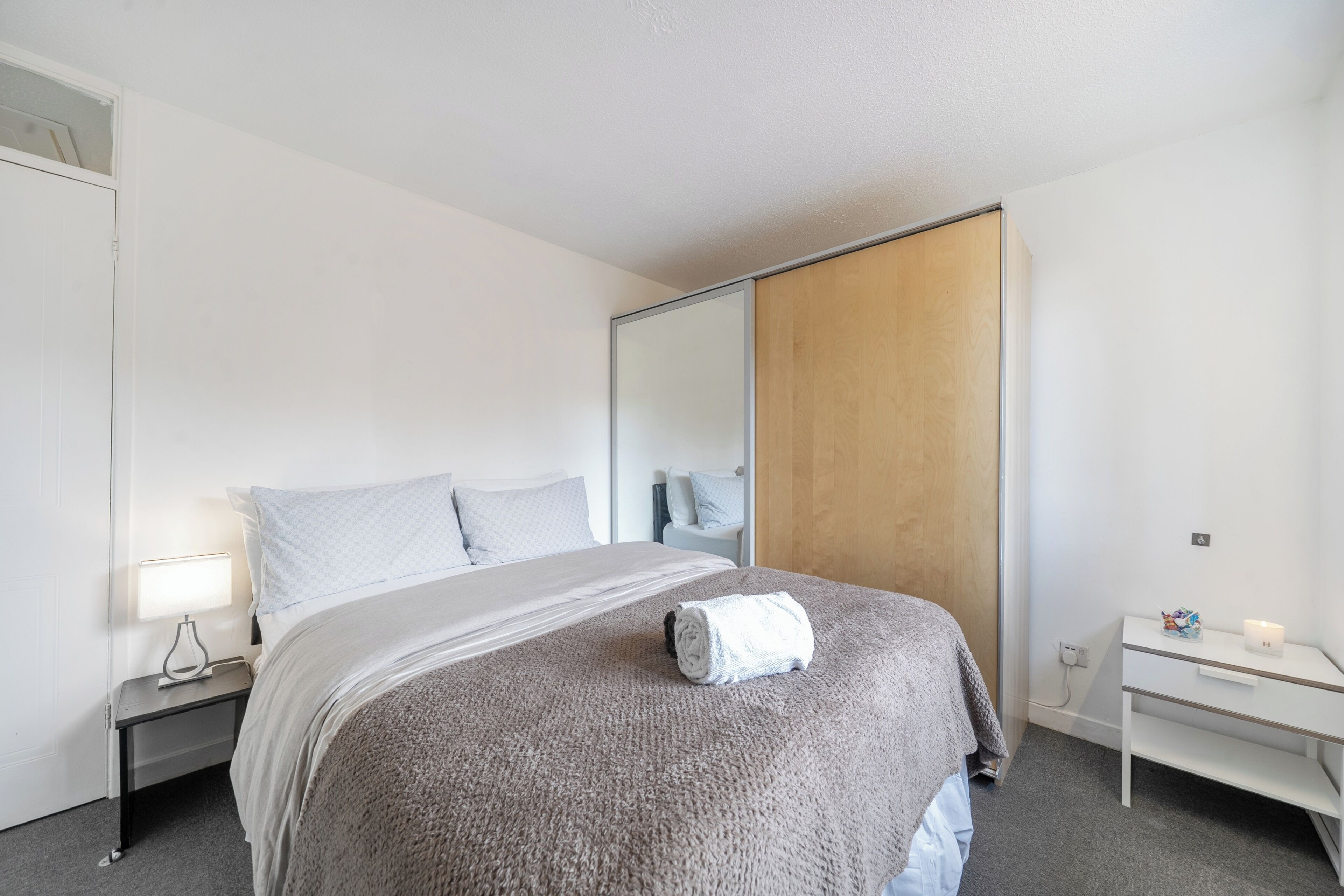 Une chambre d’hôtel avec un lit, une table de chevet avec une lampe, une armoire en bois et une petite table de chevet avec une bougie.