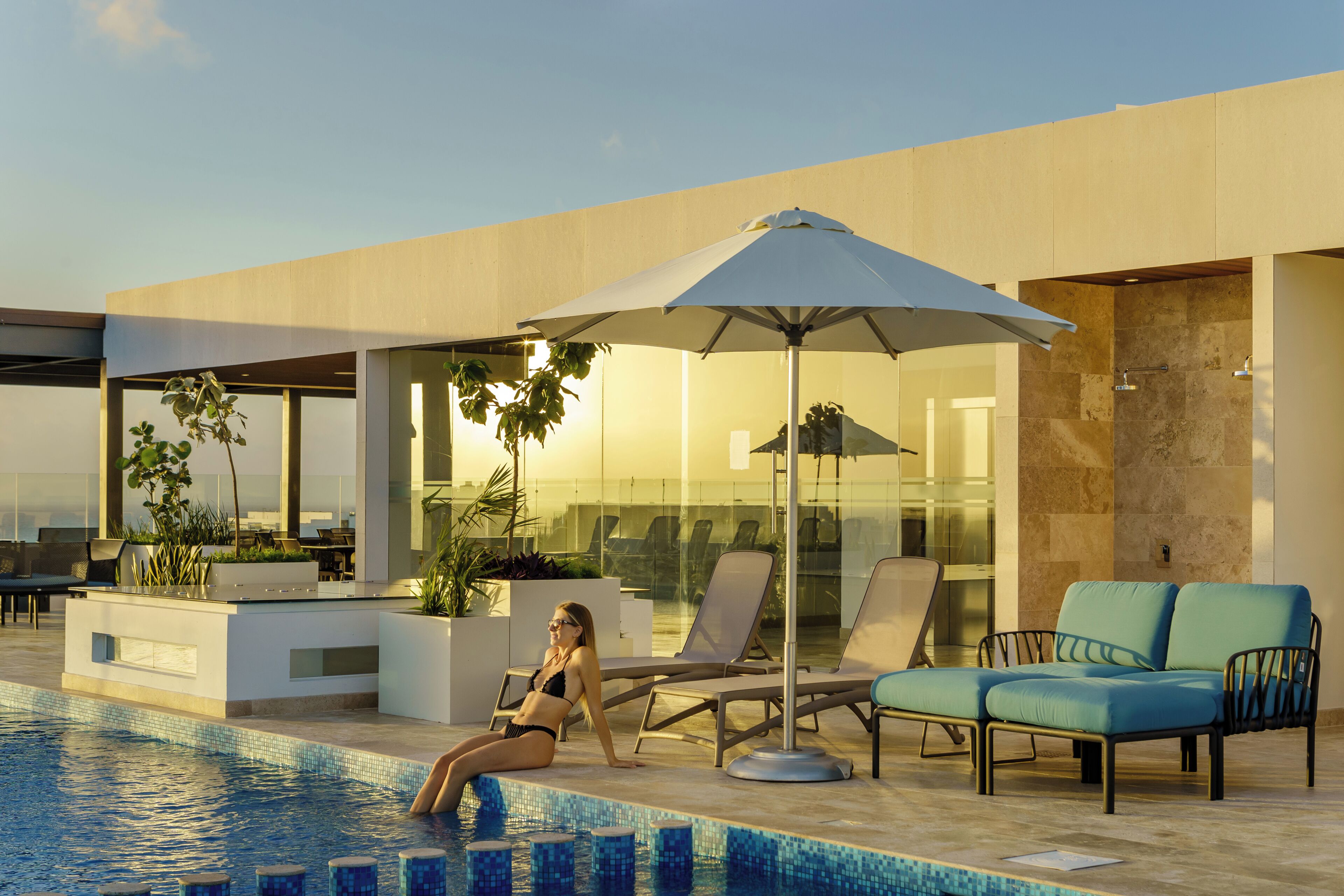 A modern pool area with lounge chairs, a large umbrella, and a view of the cityscape.