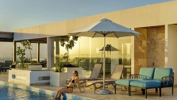 A modern pool area with lounge chairs, a large umbrella, and a view of the cityscape.