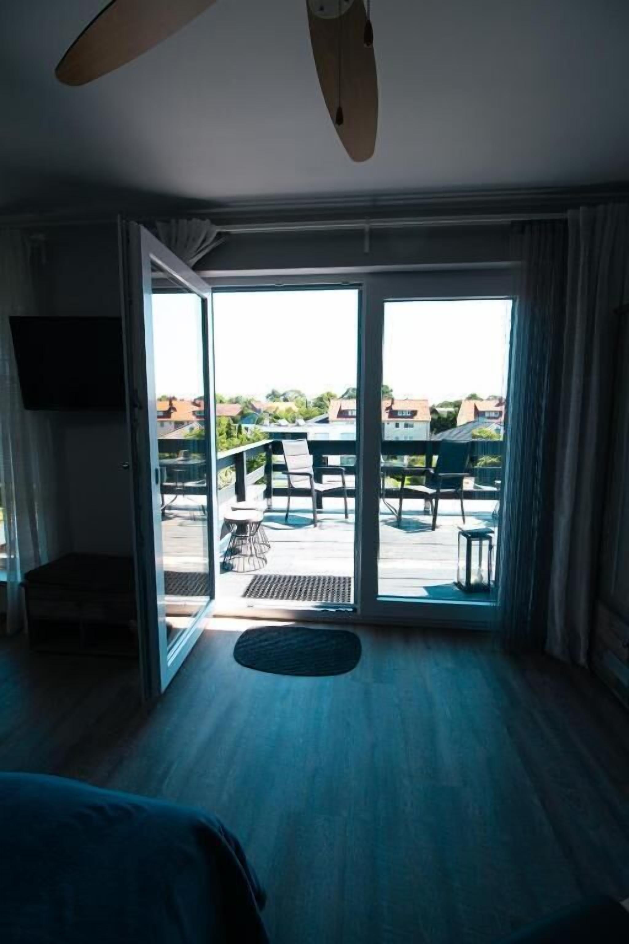 A hotel room with a bed, a ceiling fan, a television, and a sliding glass door leading to an outdoor area with a table and chairs.