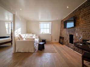 Ein modernes Wohnzimmer mit einer Couch, einem kleinen Tisch, einem Kamin und einem an einer Ziegelwand befestigten Fernseher.