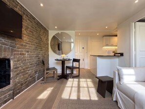 Ein Zimmer mit Backsteinwand, einem runden Spiegel, einem Esstisch mit Stühlen, einem Sofa und einem kleinen Nachttisch.