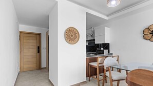 Una cucina moderna con forno a microonde, fornello e cappa aspirante. È presente una zona pranzo con tavolo in vetro e sedie in legno.