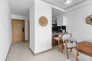 A modern kitchen with a microwave, stove, and ventilation hood. There is a dining area with a glass table and wooden chairs. - NOK Caribbean 1BR Retreat By Vistacana (Punta Cana)