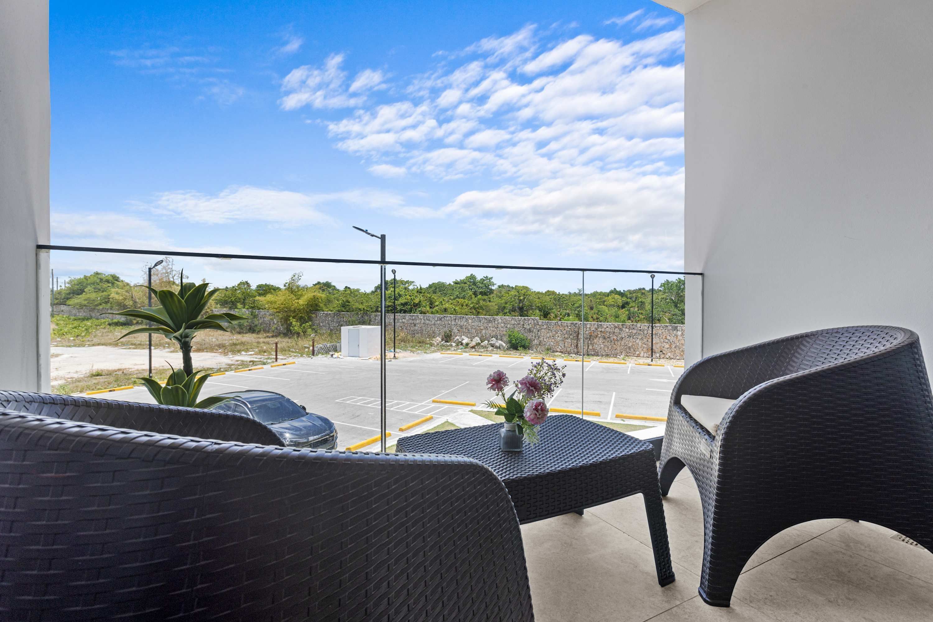 A balcony with wicker furniture, a parking area, and a clear view of the sky.