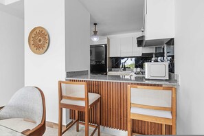 A modern kitchen with a wooden bar counter, two bar stools, and a decorative wall piece. - NOK Caribbean 1BR Retreat By Vistacana (Punta Cana)