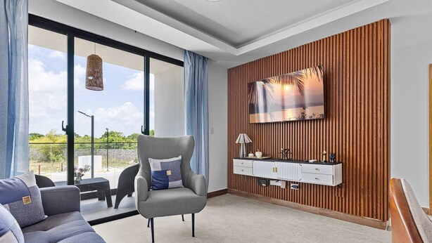Un soggiorno moderno con un divano grigio, una poltrona, una TV montata su una parete rivestita in legno e un balcone con vista sul verde.