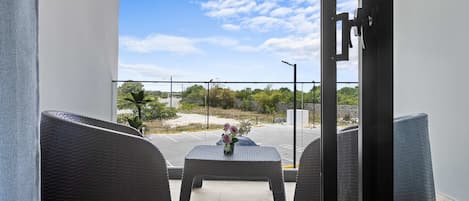 A balcony with wicker chairs, a small table with a vase, and a clear view of a parking lot and greenery.