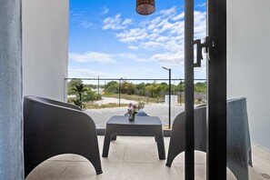 A balcony with wicker chairs, a small table with a vase, and a clear view of a parking lot and greenery. - NOK Caribbean 1BR Retreat By Vistacana (Punta Cana)