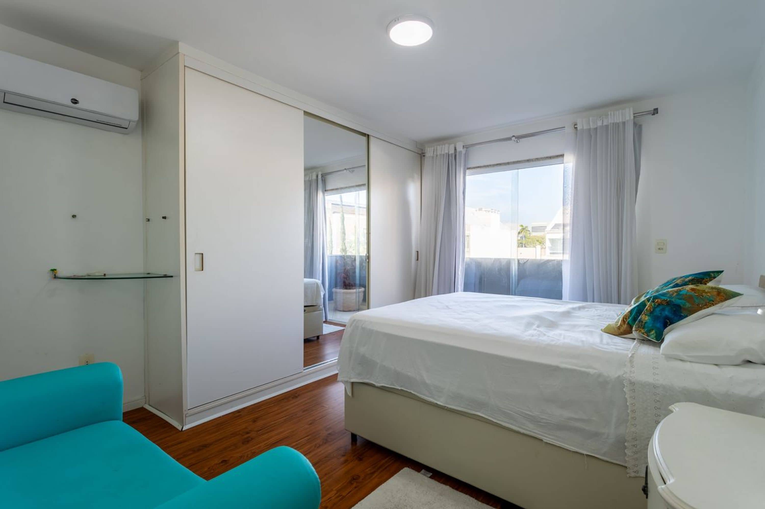 A bedroom with a bed, a wardrobe, a window with curtains, and a bathroom.