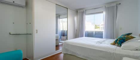A bedroom with a bed, a wardrobe, a window with curtains, and a bathroom.
