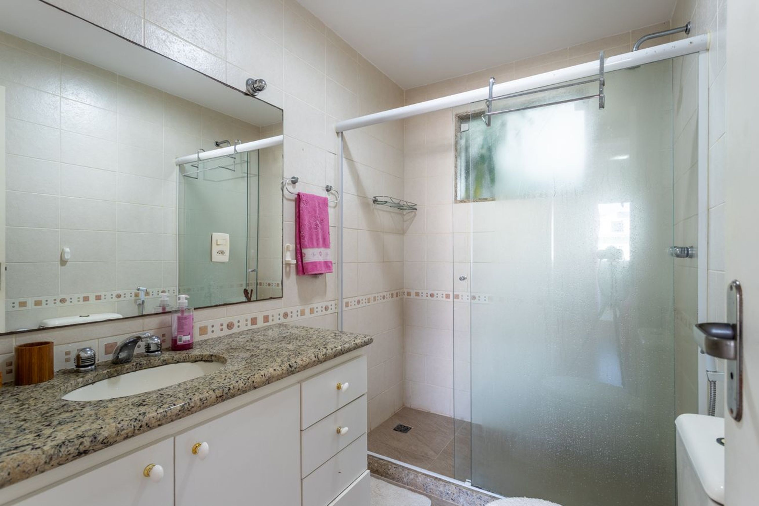 A bathroom with a granite countertop, a white sink, a mirror, a glass shower enclosure, and a toilet.
