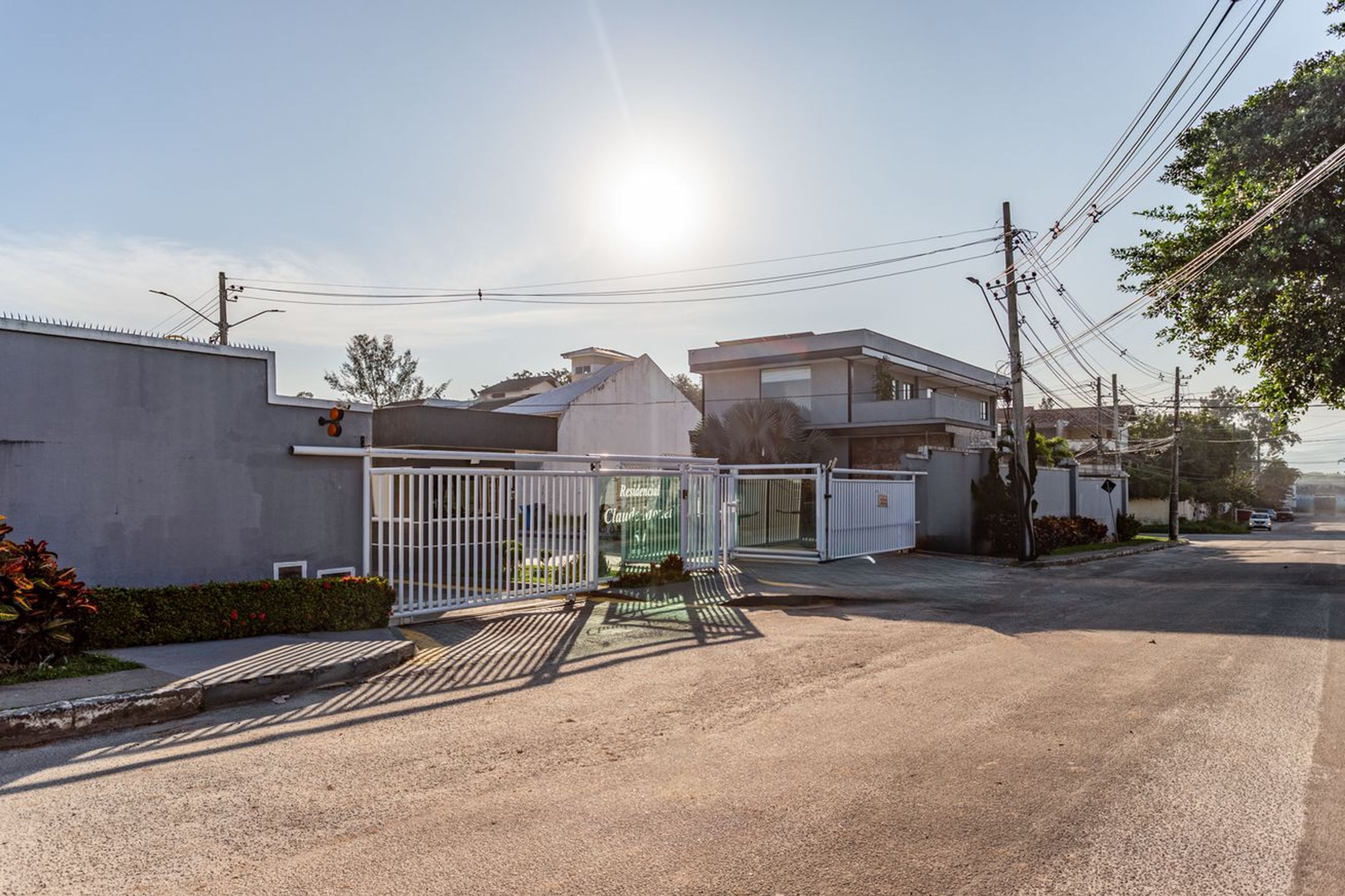 Una calle residencial con casas, una entrada vigilada y postes de electricidad.