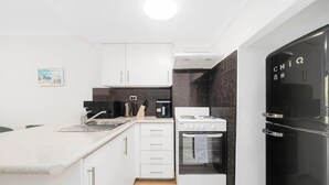 Cozinha compacta com armários brancos, bancada preta, fogão e geladeira.