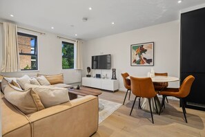 A modern living room with a sofa, a dining table with chairs, a flat-screen TV, and artwork on the wall. - 2-bed 1 Bath Sleeps 4 Putney Near Thames (London)
