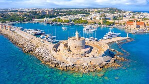 A coastal town with a historic fortification surrounded by clear blue waters, a marina with boats, and a distant cityscape. - Elegant Spacious Apartment in Rhodes With Balcony (Rhodes)