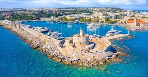 A coastal town with a historic fortification surrounded by clear blue waters, a marina with boats, and a distant cityscape. - Elegant Spacious Apartment in Rhodes With Balcony (Rhodes)