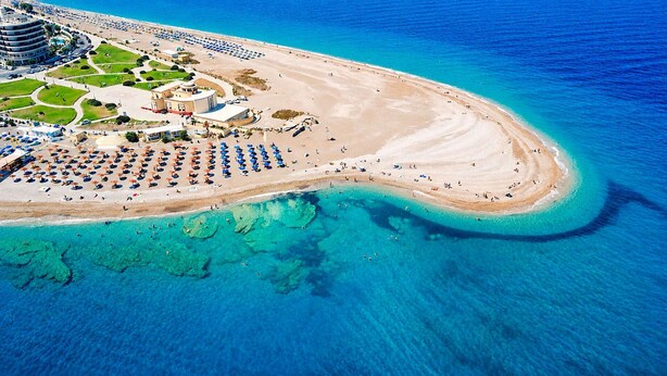 An aerial view of a coastal resort with a sandy beach, clear blue waters, and a marina with boats. - Elegant Spacious Apartment in Rhodes With Balcony (Rhodes)