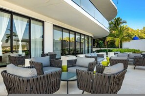 A modern outdoor seating area with wicker furniture and glass tables, overlooking a landscaped garden with palm trees. - Beachfront Luxury at Tizate Pool Concierge (La Cruz de Huanacaxtle)